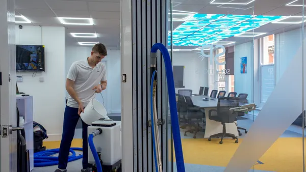 Technician filling hot water extraction equipment before cleaning a commercial office carpet