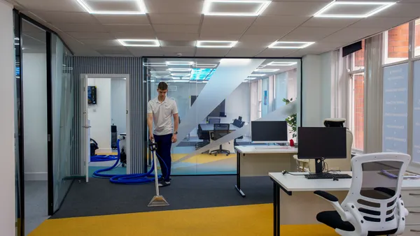 Technician cleaning office carpet between desks with a hot water extraction wand