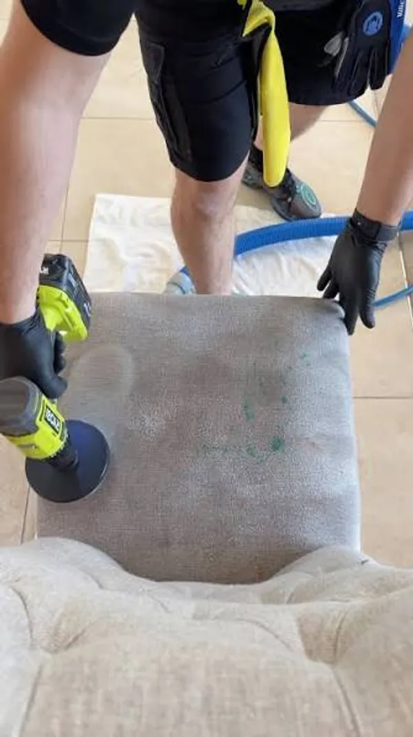 A stained fabric seat being agitated with a rotary brush during a sofa deep clean