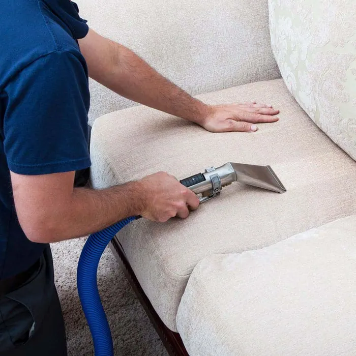 Technician deep cleaning a cream fabric sofa seat with an upholstery extraction tool